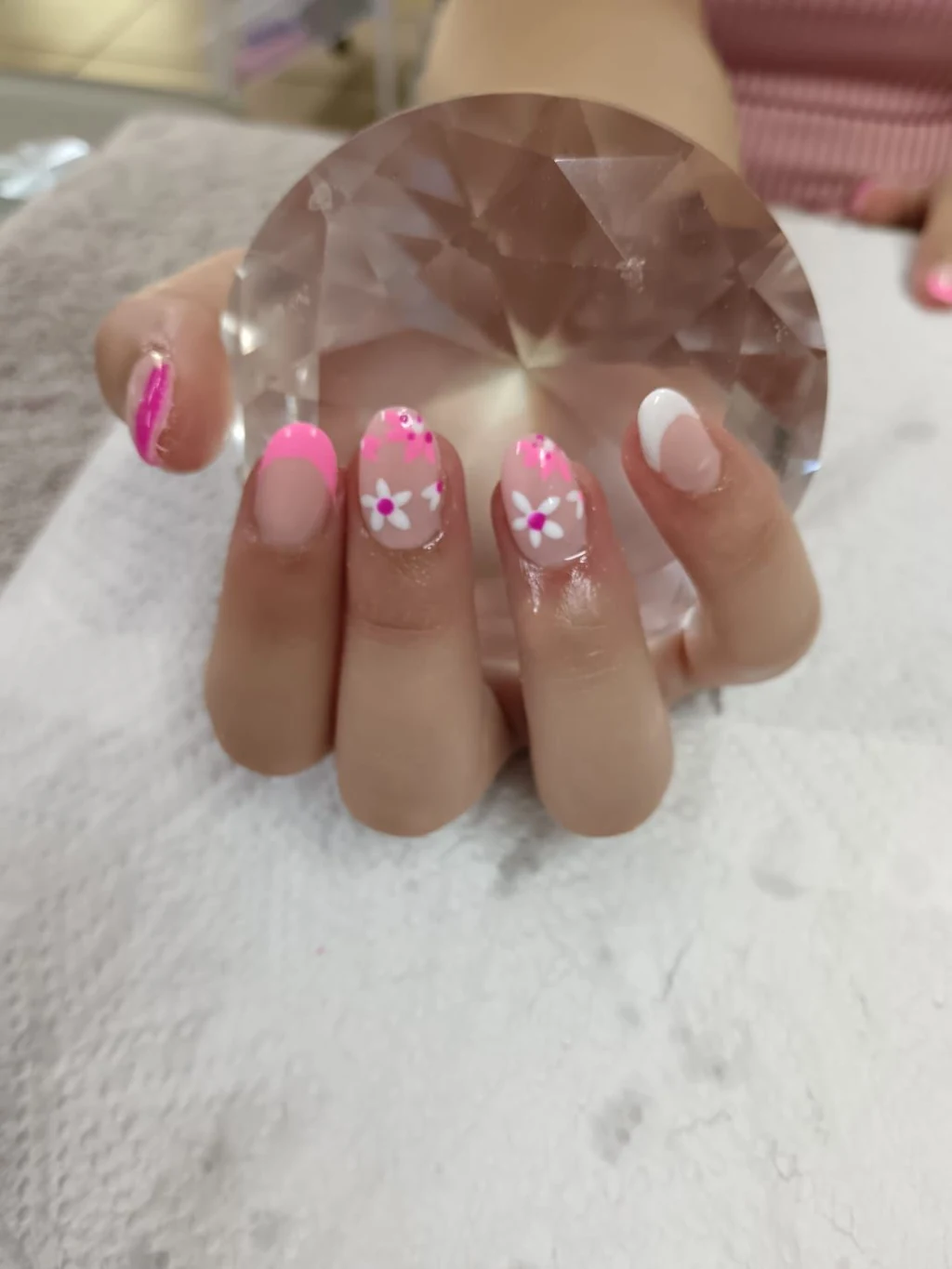 Soft pink nails with hand-painted daisies, held over a crystal